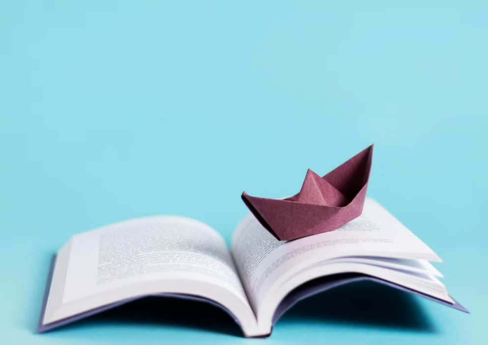 an open book with a dark-red paper boat on it