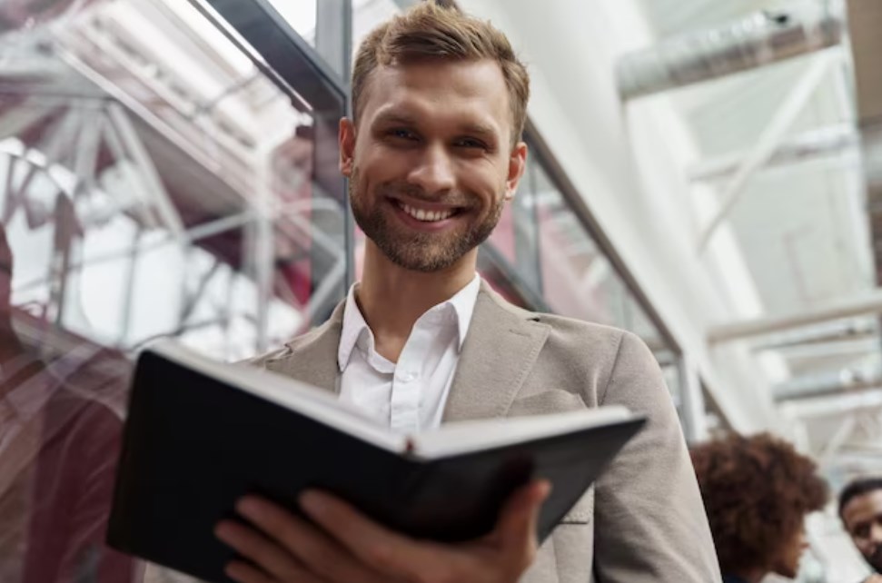 a smiling bearded businessman holding an open book and looking at the camera