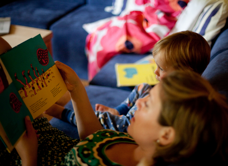 a mother and a toddler reading a book while lying on the bed