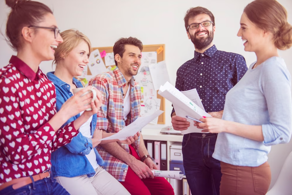 group of people talk and smile, three of them holding papers