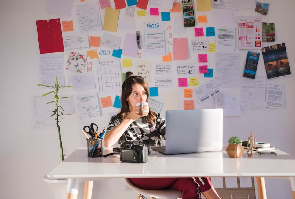 woman drinks coffee and watches on the laptop, notes and paper behind her on the wall